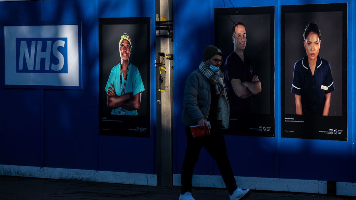 A pedestrian passes portraits of National Health Service (NHS) workers on hoardings outside a temporary structure on Friday, Jan. 7, 2022. (Chris J. Ratcliffe/Bloomberg via Getty Images)