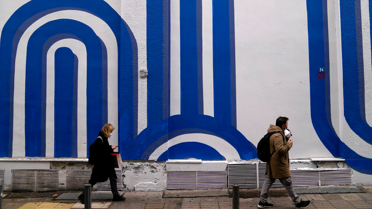 Pedestrians wearing face masks to curb the spread of coronavirus pass in front of the mural "Waves" by the artist Adioshpe in Athens, Greece, Wednesday, Jan. 12, 2022.