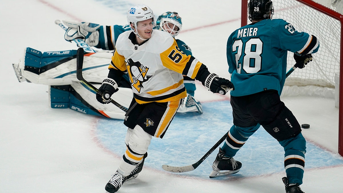 Pittsburgh Penguins left wing Jake Guentzel, left, celebrates after scoring in front of San Jose Sharks goaltender Adin Hill, rear, and right wing Timo Meier (28) during overtime of an NHL hockey game in San Jose, Calif., Saturday, Jan. 15, 2022. The Penguins won 2-1.