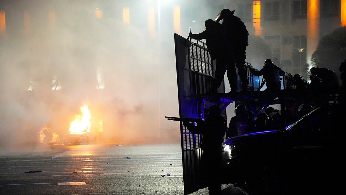 A police car on fire as riot police prepare to stop protesters in the center of Almaty, Kazakhstan, Wednesday, Jan. 5, 2022.