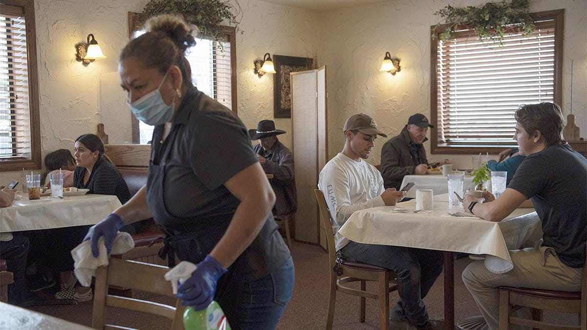 A worker wearing a protective mask and gloves disinfects tables at Pecos River Cafe in Carlsbad, New Mexico, U.S., on Friday, Sept. 11, 2020.