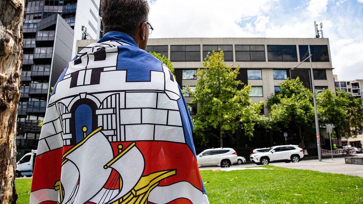 A supporter of Novak Djokovic wears a Serbian flag as he waits outside Park Hotel where Djokovic was taken pending his removal from the country after his visa was canceled by the Australian Border Force on January 06, 2022 in Melbourne, Australia.