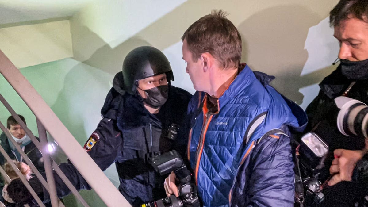 A police officer pushes photographers from a door of the apartment where Oleg Navalny, brother