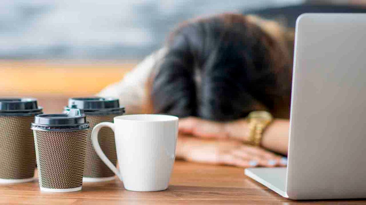 a person with their head down in front of a laptop computer and cups of coffee