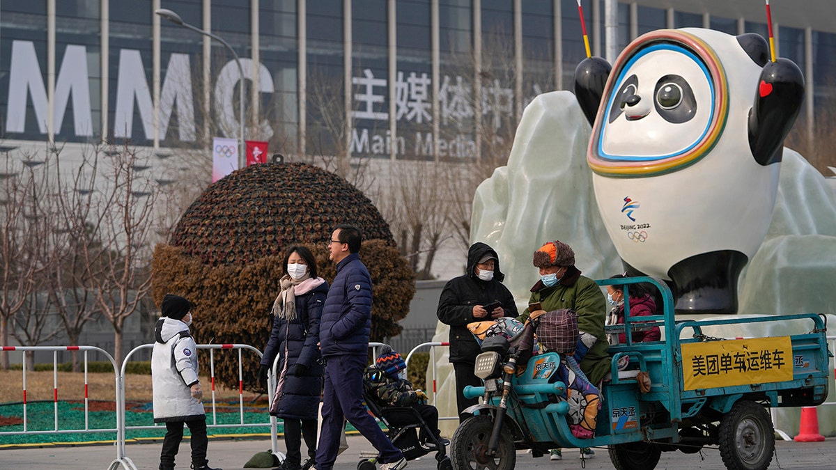 People wearing face masks to protect from the coronavirus walk by a Beijing Winter Olympics mascot on display near the barricaded Main Press Center (MPC) in Beijing, Wednesday, Jan. 19, 2022. 