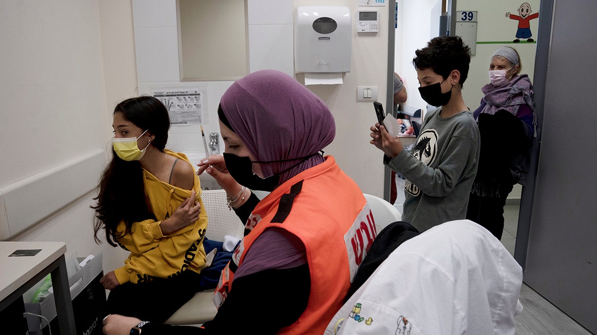N'amah Yetzhak Abohaikal, a volunteer with the women's unit of United Hatzalah emergency service, prepares administer the COVID-19 vaccine to a teen girl as her brother and grandmother watch, at Clalit Health Services in Mevaseret Zion, Tuesday, Jan. 11, 2022. 