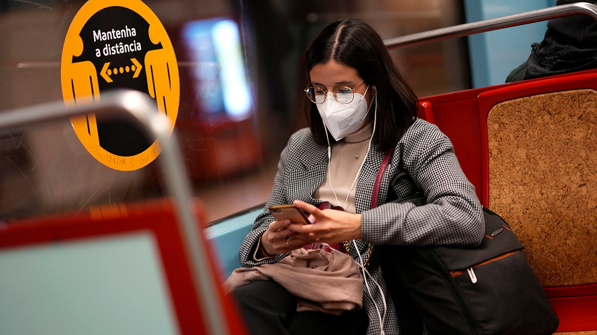 A young woman wearing a face mask looks at her phone on a subway train in Lisbon, Jan. 6, 2022. 