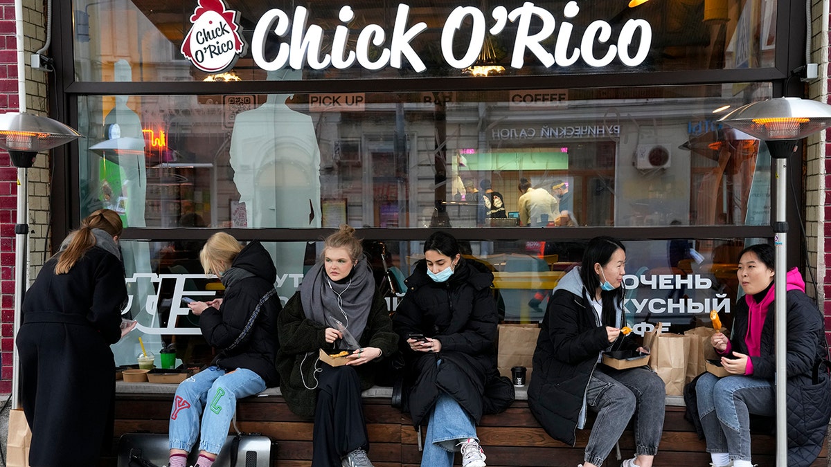 People eat their takeaway food sitting outside a cafe that is closed due to coronavirus in Moscow, Russia, Friday, Oct. 29, 2021. 