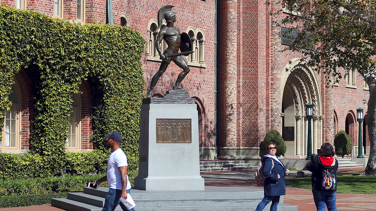 In this March 12, 2019, file photo, people pose for photos in front of the iconic Tommy Trojan statue on the campus of the University of Southern California in Los Angeles. 