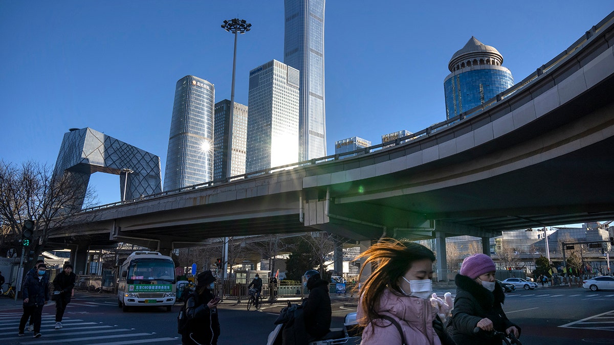 Commuters wearing face masks to help protect against the coronavirus walk across an intersection in the central business district in Beijing, Thursday, Jan. 13, 2022. 