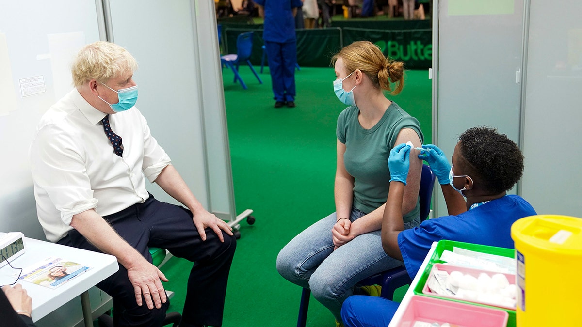 Britain's Prime Minister Boris Johnson, left, watches Esther receive her COVID-19 booster vaccine in the at Stoke Mandeville Stadium in Aylesbury, England, Monday Jan. 3, 2022. 