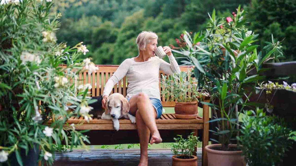 A woman drinking coffee outdoors with her dog