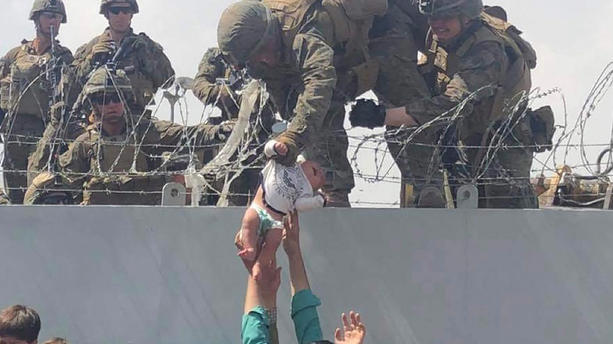 This image made available to AFP on August 20, 2021 by Human Rights Activist Omar Haidari, shows a US Marine grabbing an infant over a fence of barbed wire during an evacuation at Hamid Karzai International Airport in Kabul on August 19, 2021. - A Pentagon official confirmed Friday that US evacuation operations from Kabul's airport have been stalling because the receiving base in Qatar is overflowing and could not receive evacuees. "There has been a considerable amount of time today where there haven't been departures," Brigadier General Dan DeVoe of the US Air Mobility Command told reporters