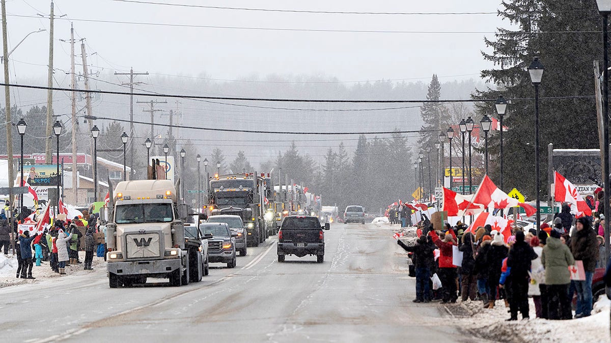 Protesters and supporters against a COVID-19 vaccine mandate for cross-border truckers cheer as a parade of trucks and vehicles pass through Kakabeka Falls outside of Thunder Bay, Ontario, on Wednesday, Jan. 26, 2022. (David Jackson/The Canadian Press via AP)