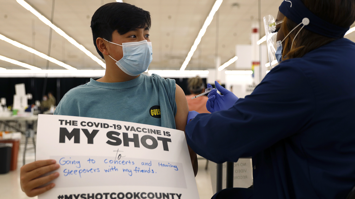 A 13-year-old boy holds a sign in support of COVID-19 vaccinations as he receives his first Pfizer vaccination at the Cook County Public Health Department.