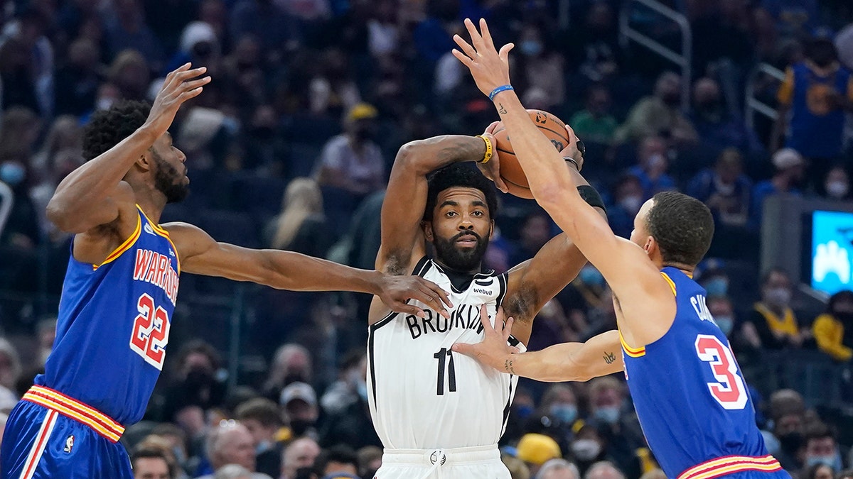 Brooklyn Nets guard Kyrie Irving (11) looks to pass the ball between Golden State Warriors forward Andrew Wiggins (22) and guard Stephen Curry during the first half of an NBA basketball game in San Francisco, Saturday, Jan. 29, 2022.