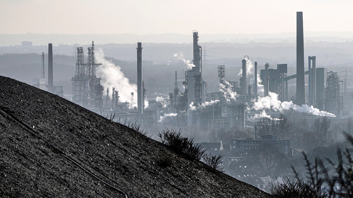 An oil refinery smokes behind a former coal mine dump in Gelsenkirchen, Germany, Monday, Jan. 10, 2022.