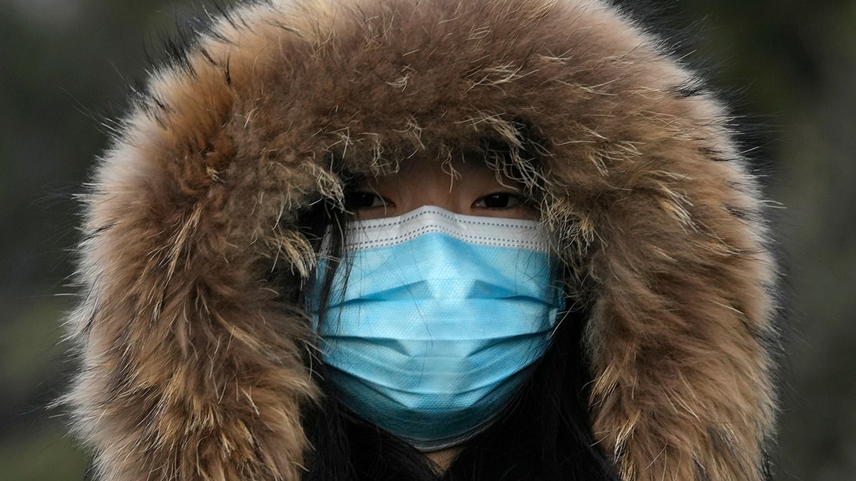 A woman wearing a mask to curb the spread of the coronavirus walks along a street in Beijing, China, Tuesday, Jan. 4, 2022
