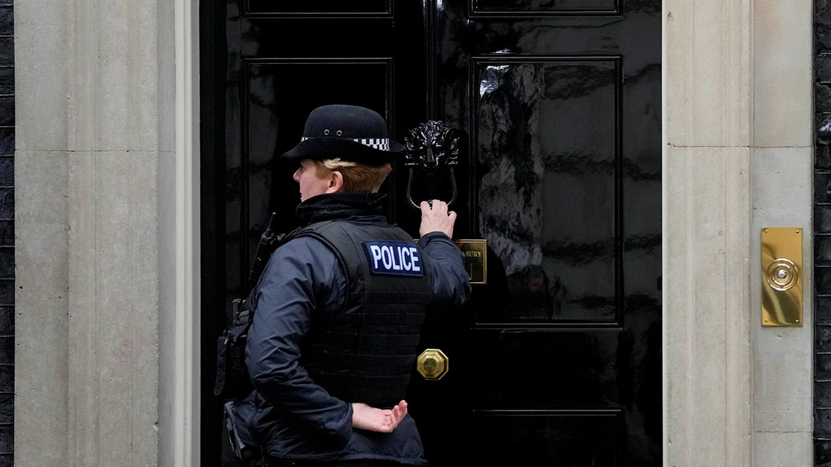 A police officer knocks on the door to 10 Downing Street in London, Tuesday, Jan. 11, 2022. 