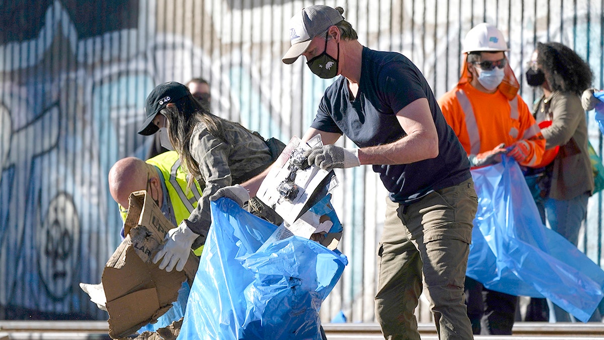 California Gov. Gavin Newsom, center, removes cardboard and other discarded items from a Union Pacific Railroad site