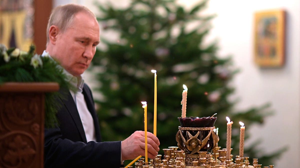 Russian President Vladimir Putin lights a candle during the Orthodox Christmas Liturgy in Novo-Ogaryovo, outside Moscow, Russia, late Thursday, Jan. 6, 2022. (Alexei Nikolsky/Sputnik, Kremlin Pool Photo via AP)