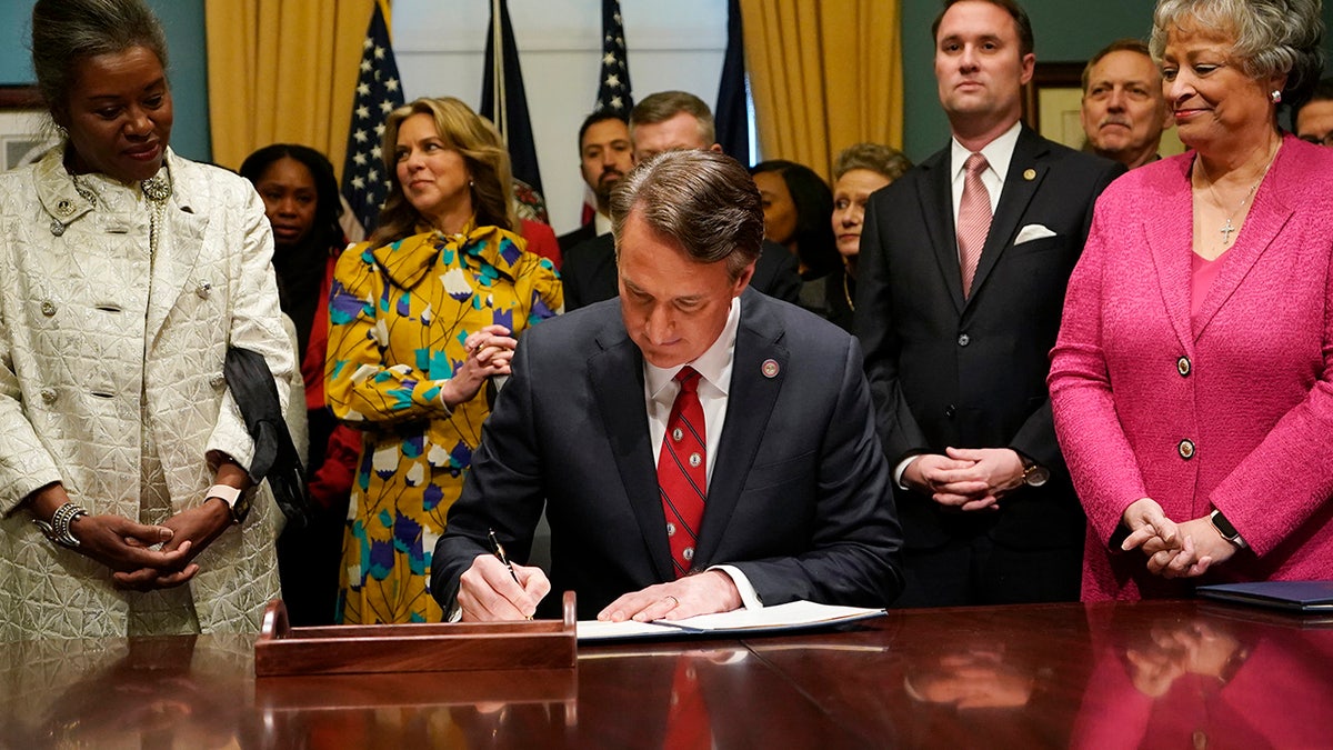 Gov. Glenn Youngkin, center, signs executive orders at the Capitol