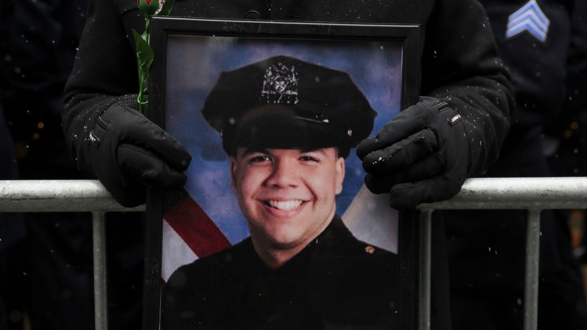 A New York Police officer holds a photo of Officer Jason Rivera while gathering for Rivera's funeral service, Friday, Jan. 28, 2022, outside St. Patrick's Cathedral in New York. (AP Photo/Yuki Iwamura)