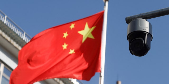 FILE PHOTO: A security surveillance camera overlooking a street is pictured next to a nearby fluttering flag of China in Beijing, China November 25, 2021. REUTERS/Carlos Garcia Rawlins