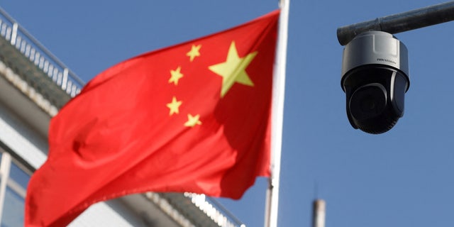 FILE PHOTO: A security surveillance camera overlooking a street is pictured next to a nearby fluttering flag of China in Beijing, China November 25, 2021. REUTERS/Carlos Garcia Rawlins