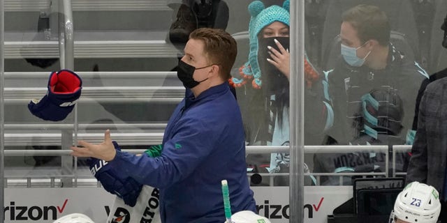 Seattle Kraken fan Nadia Popovici, center, reacts after she was introduced along with Vancouver Canucks assistant equipment manager Brian "Red" Hamilton, standing, during the first period of an NHL hockey game Saturday, Jan. 1, 2022, in Seattle. 