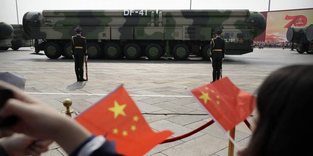 Spectators wave Chinese flags as military vehicles carrying DF-41 nuclear ballistic missiles roll during a parade to commemorate the 70th anniversary of the founding of Communist China in Beijing on Oct. 1, 2019. 