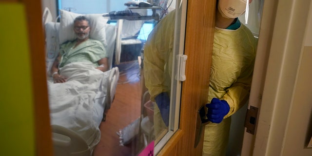 Registered nurse Rachel Chamberlin, of Cornish, N.H., right, steps out of an isolation room where where Fred Rutherford, of Claremont, N.H., left, recovers from COVID-19 at Dartmouth-Hitchcock Medical Center, in Lebanon, N.H. (AP Photo/Steven Senne)