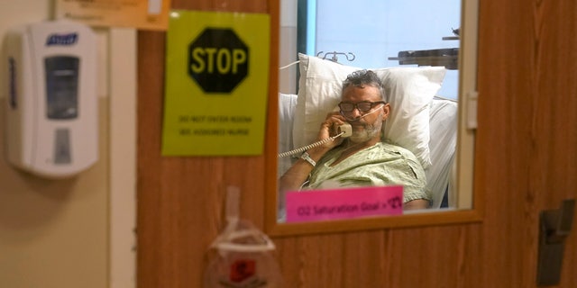 Patient Fred Rutherford, of Claremont, N.H., who is recovering from COVID-19, speaks on a telephone with a reporter from The Associated Press from an isolation room at Dartmouth-Hitchcock Medical Center, in Lebanon, N.H. (AP Photo/Steven Senne)