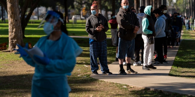 People wait in line for a COVID-19 test as medical assistant Leslie Powers, foreground, distributes test results at a testing site in Long Beach, Calif., Thursday, Jan. 6, 2022. (AP Photo/Jae C. Hong)