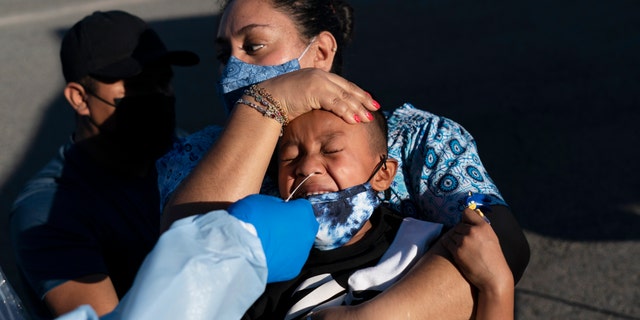 Reina Monterrosa holds the head of her 6-year-old son, Anderson, as nurse practitioner Rita Ray collects a nasal swab sample for a COVID-19 test at Families Together of Orange County community health center in Tustin, Calif., jueves, ene. 6, 2022. (Foto AP/Jae C. hongo)