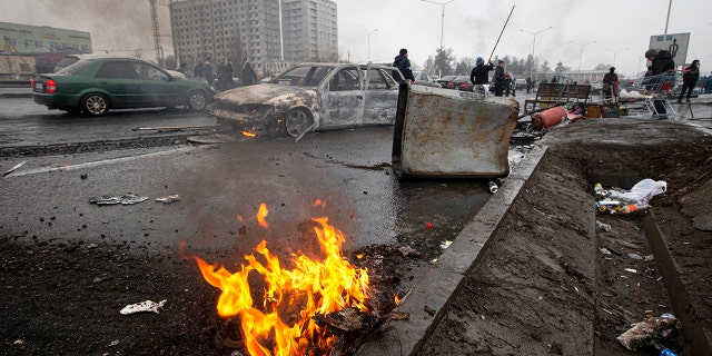 People walk past cars, which were burned after clashes, on a street in Almaty, Kazakhstan, Friday, Jan. 7, 2022.