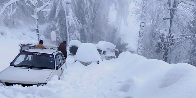 People walk past vehicles trapped in a heavy snowfall-hit area in Murree, some 28 miles (45 kilometers) north of the capital of Islamabad, Pakistan, Saturday, Jan. 8, 2022. (Inter Services Public Relations via AP)