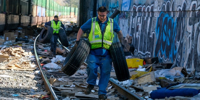 Workers Adam Rodriguez, front, and Luis Rosas pick up vehicle tires from the shredded boxes and packages at a section of the Union Pacific train tracks in downtown Los Angeles Friday, Jan. 14, 2022. (AP Photo/Ringo H.W. Chiu)
