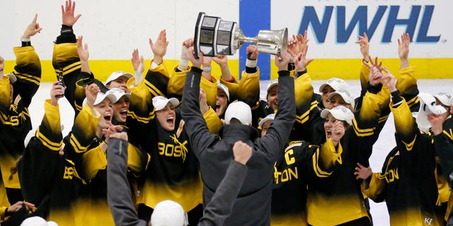 Boston Pride players cheer as coach Paul Mara hoists the NWHL Isobel Cup trophy after the team's win over the Minnesota Whitecaps in the championship hockey game in Boston, Saturday, March 27, 2021. 