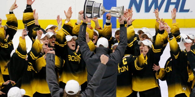 Boston Pride players cheer as coach Paul Mara hoists the NWHL Isobel Cup trophy after the team's win over the Minnesota Whitecaps in the championship hockey game in Boston, Saterdag, Maart 27, 2021.