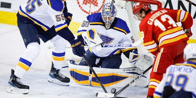 S t. Louis Blues' Colton Parayko, izquierda, and Calgary Flames' Johnny Gaudreau, derecho, battle for the puck as Blues goalie Jordan Binnington looks on during second-period NHL hockey game action in Calgary, Alberta, lunes, ene. 24, 2022.