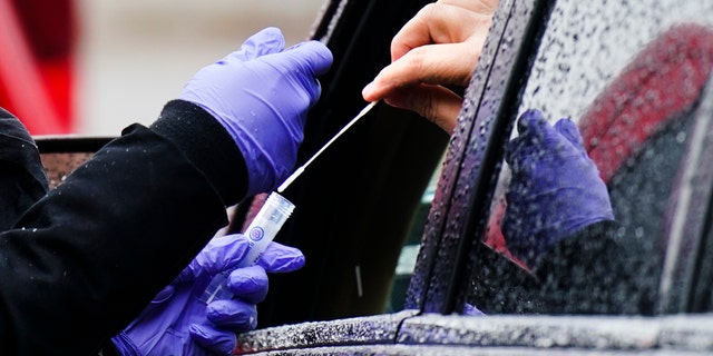 A driver places a swab into a vial at a free drive-thru COVID-19 testing site in the parking lot of the Mercy Fitzgerald Hospital in Darby, Pennsylvania. 