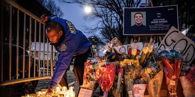 A New York City Police Department officer lights a candle at a makeshift memorial outside the NYPD's 32nd Precinct, near the scene of a shooting that claim the lives of NYPD officers Jason Rivera and Wilbert Mora in the Harlem neighborhood of New York, Monday Jan. 24, 2022.  (AP Photo/Yuki Iwamura, File)
