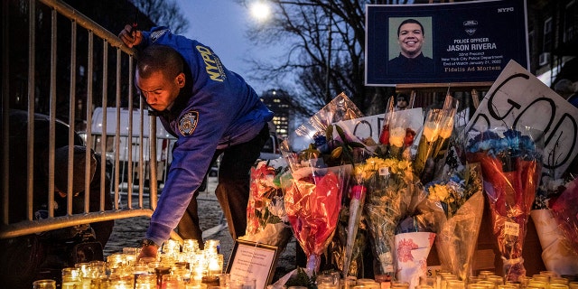 FILE - A New York City Police Department officer lights a candle at a makeshift memorial outside the NYPD's 32nd Precinct, near the scene of a shooting that claim the lives of NYPD officers Jason Rivera and Wilbert Mora in the Harlem neighborhood of New York, Monday Jan. 24, 2022.  (AP Photo/Yuki Iwamura, File)