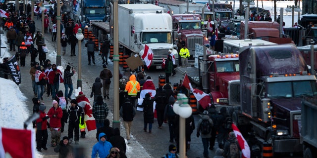 People walk beside trucks parked along Wellington Street during a rally against COVID-19 restrictions on Parliament Hill, which began as a cross-country convoy protesting a federal vaccine mandate for truckers, in Ottawa, on Saturday, Jan. 29, 2022. (Justin Tang/The Canadian Press via AP)