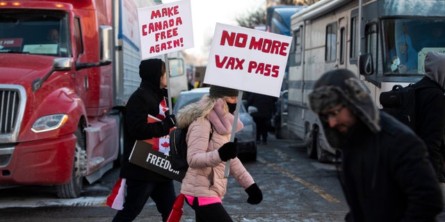People walk in front of trucks parked on Wellington Street as they join a rally against COVID-19 restrictions on Parliament Hill, which began as a cross-country convoy protesting a federal vaccine mandate for truckers, in Ottawa, on Saturday, Jan. 29, 2022. (Justin Tang/The Canadian Press via AP)