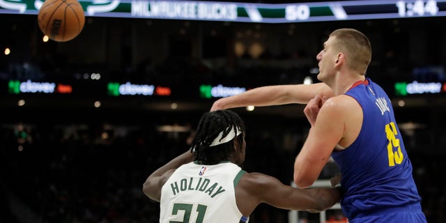 Denver Nuggets' Nikola Jokic (15) passes around Milwaukee Bucks' Jrue Holiday (21) during the first half of an NBA basketball game Sunday, Jan. 30, 2022, a Milwaukee.