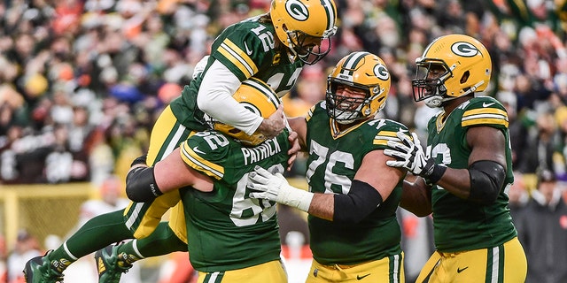Green Bay Packers quarterback Aaron Rodgers is lifted up by guard Lucas Patrick after setting the franchise record for most passing TDs on Dec 25, 2021, in Green Bay, Wisconsin.