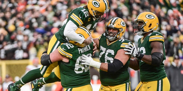 Green Bay Packers quarterback Aaron Rodgers is lifted up by guard Lucas Patrick after setting the franchise record for most passing TDs on Dec 25, 2021, in Green Bay, Wisconsin.