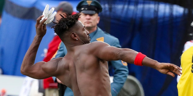 A N.J. State Police trooper, background, watches as Tampa Bay Buccaneers wide receiver Antonio Brown (81) throws his gloves into the stands while his team's offense is on the field against the New York Jets during the third quarter of an NFL football game Sunday, Jan. 2, 2022, in East Rutherford, N.J.